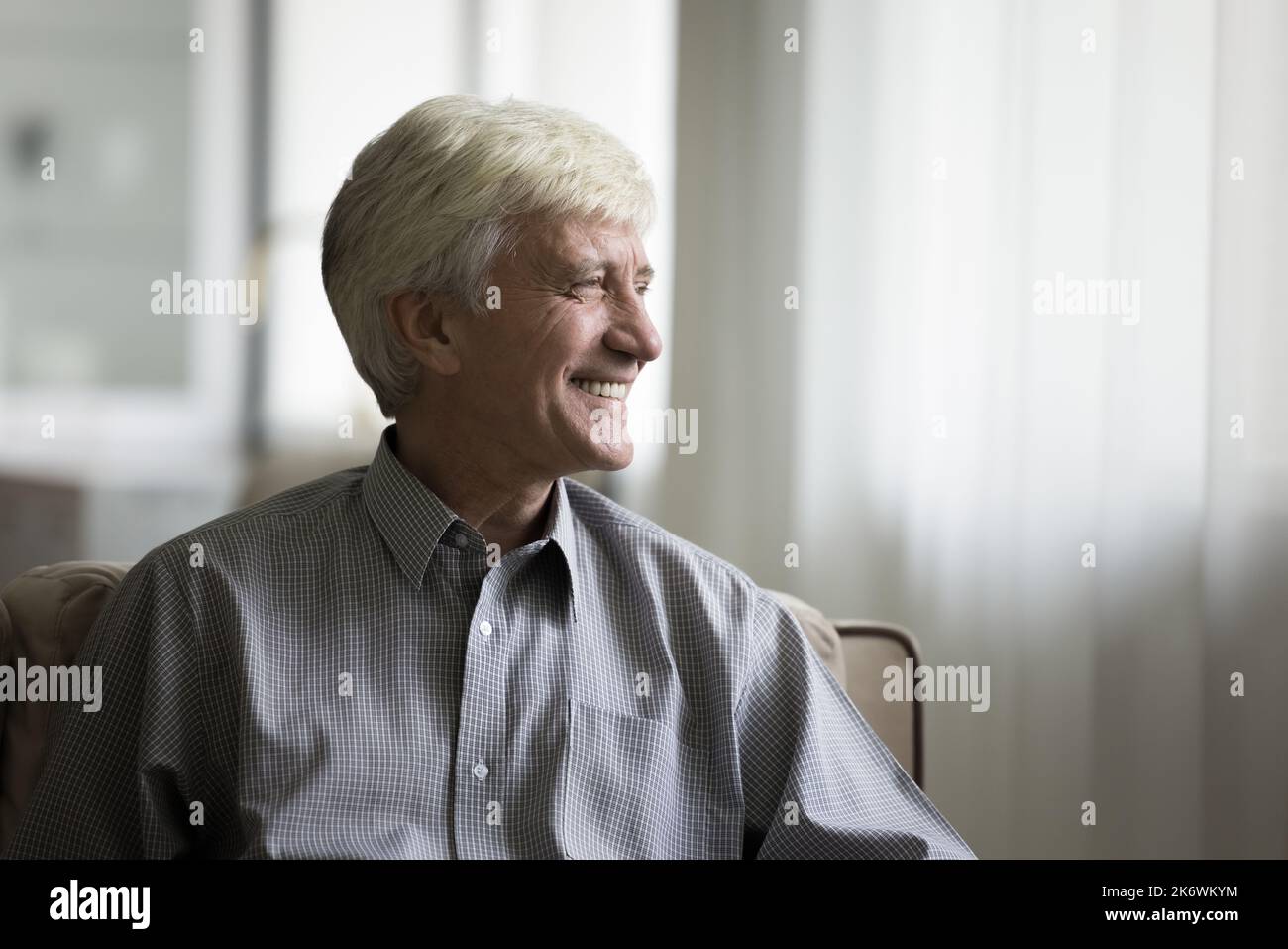 Nachdenklicher älterer Mann, der sich auf der Couch entspannt, lächelt und in die Ferne blickt Stockfoto