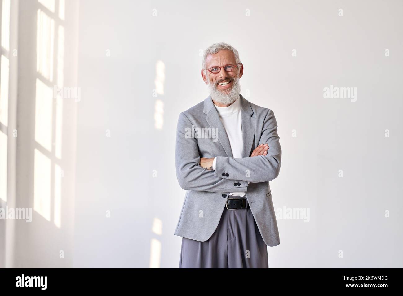 Glücklicher älterer Geschäftsmann, der Anzug trägt, der isoliert an einer weißen Wand steht. Stockfoto