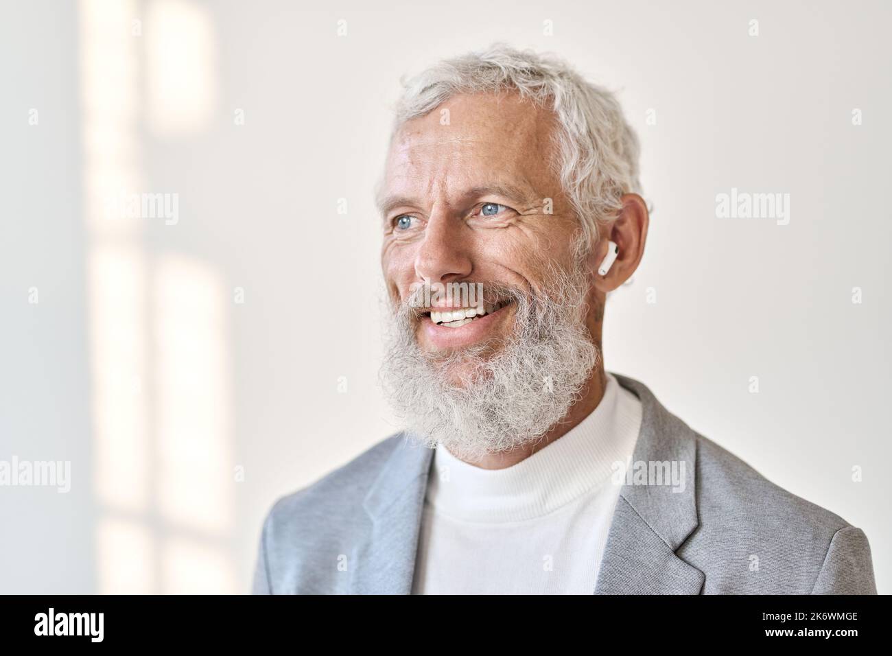 Lächelnder alter Geschäftsmann, der Ohrstöpsel trägt und Musik oder Podcast hört. Nahaufnahme Stockfoto