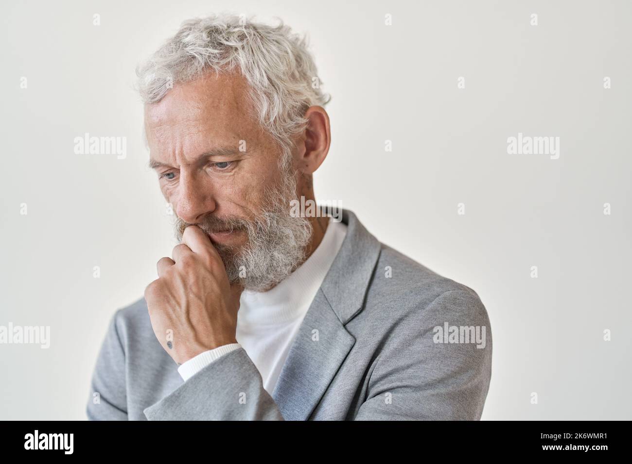 Nachdenklicher, trauriger alter Geschäftsmann, der isoliert an einer weißen Wand denkt. Stockfoto