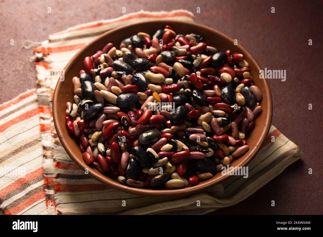 Bunte Bio-Bohnen auf burgunderrotem Hintergrund Stockfoto