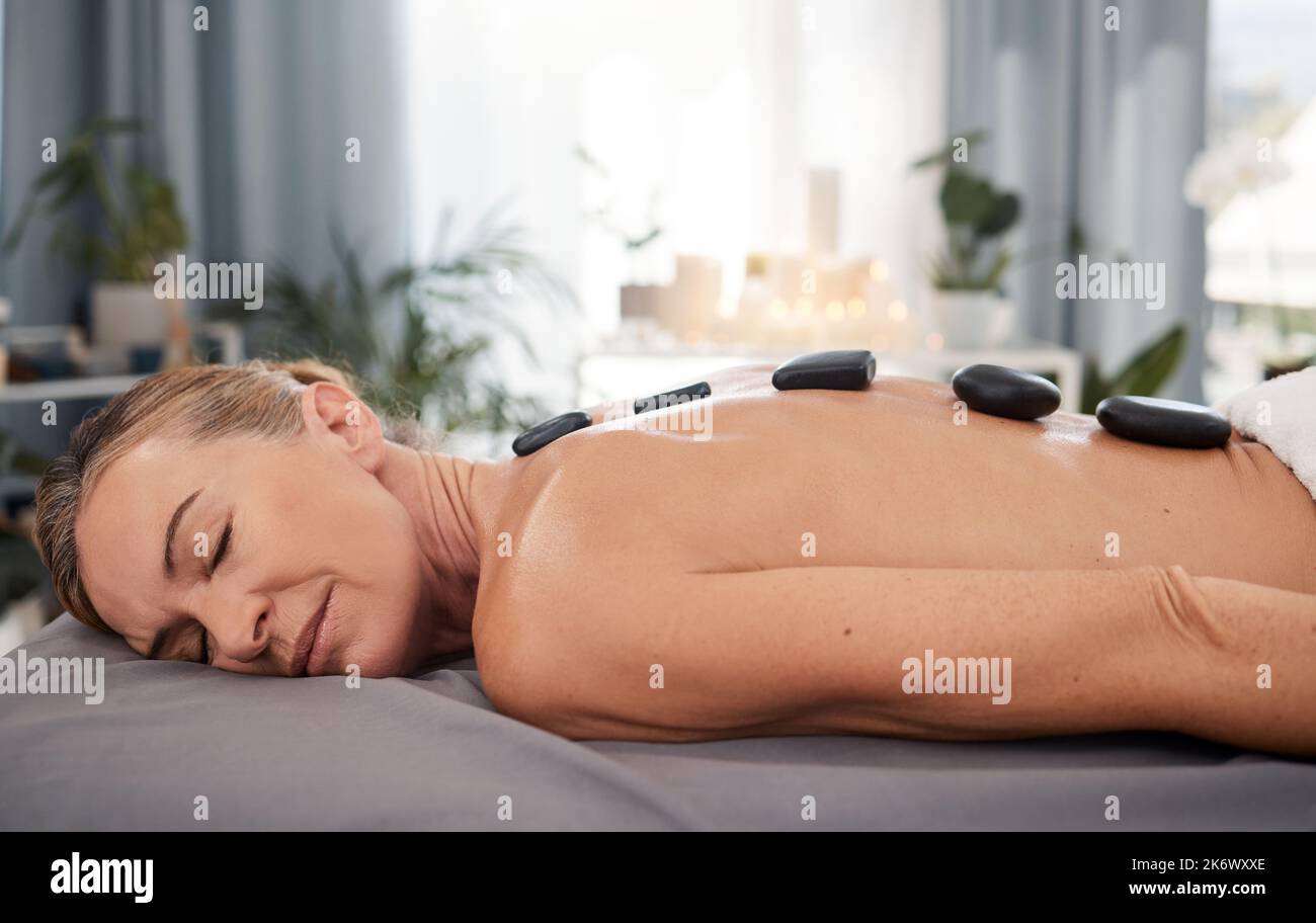 Nach dieser heißen Steinmassage werden Sie besser schlafen. Eine reife Frau genießt eine entspannende Hot Stone Massage in einem Spa. Stockfoto