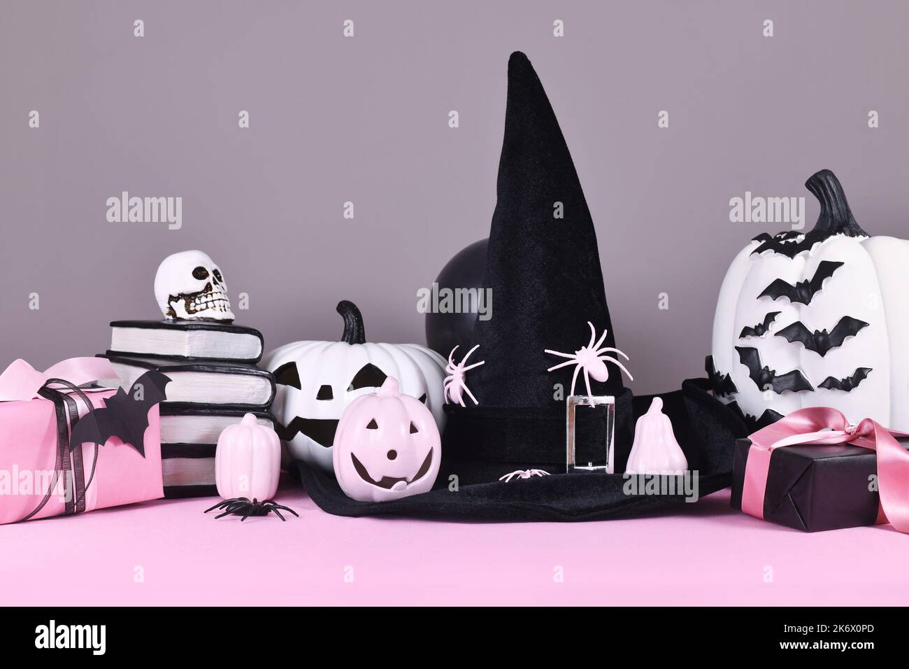 Pink-weißes Halloween Dekor mit schwarzen und weißen Kürbissen, Hexenhut und Zauberbüchern auf grauem Hintergrund Stockfoto
