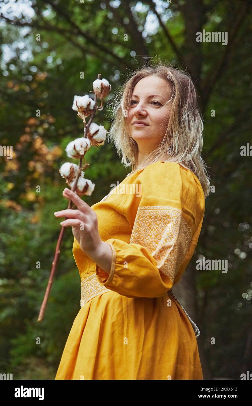 Schöne ukrainische Frau in besticktem Kleid hält einen Zweig aus Baumwolle Stockfoto