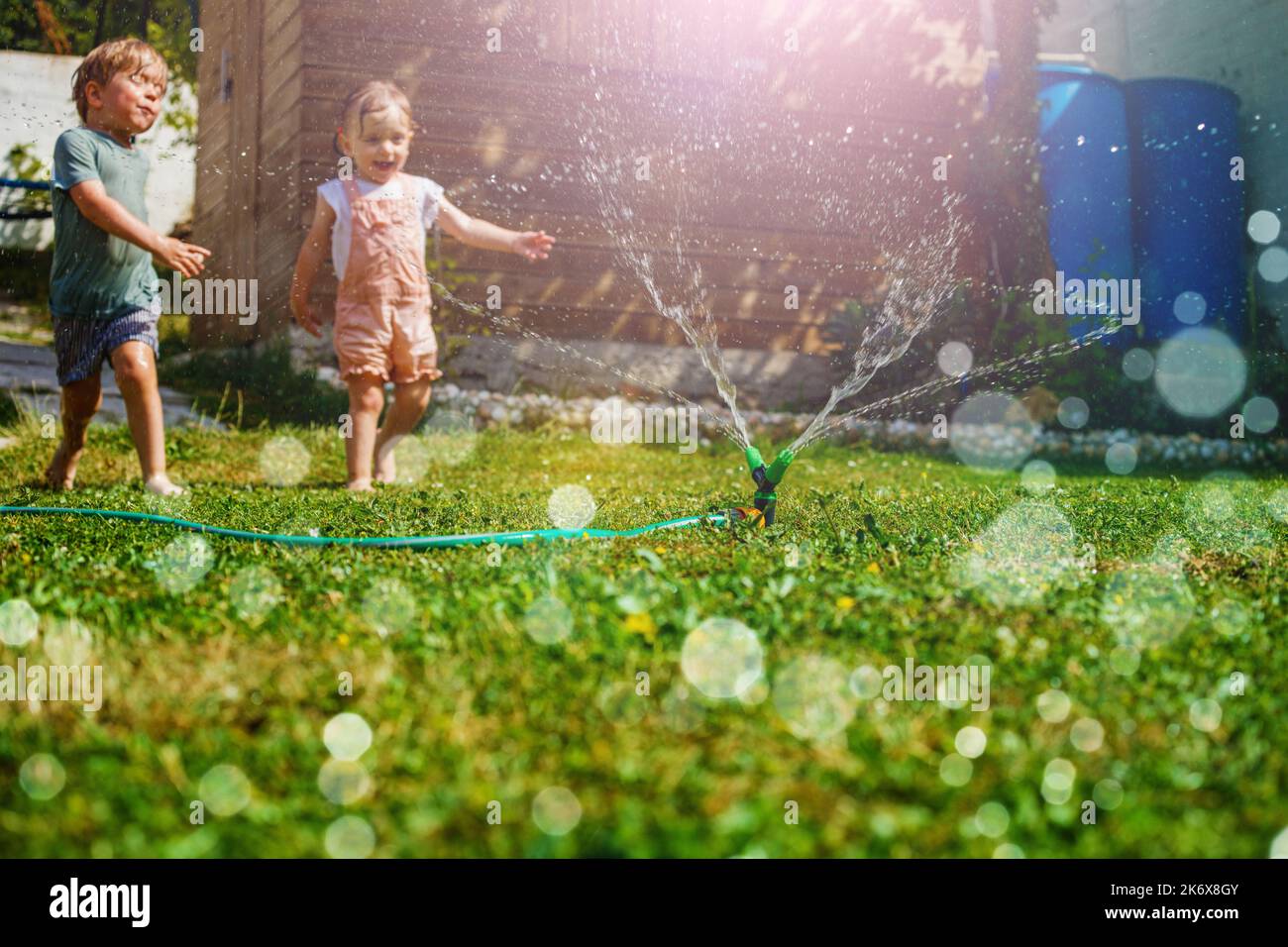 Zwei Kinder haben Spaß im Garten - spielen mit Wasser auf der Wiese Stockfoto