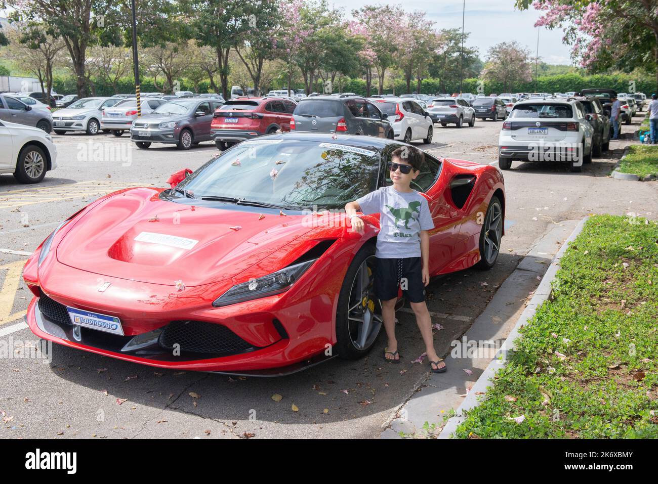 Atibaia - Brasilien, 7. Oktober 2022: Junge in Sonnenbrille posiert neben einem geparkten roten Ferrari F8 Tributo. Mittelmotor-Sportwagen mit Heckantrieb. Ferrari - Ital Stockfoto