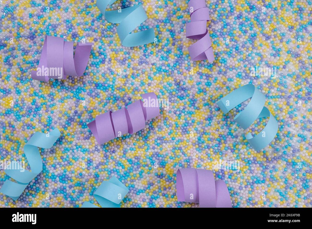 Festlicher mehrfarbiger Hintergrund in zarten Pastellfarben mit Prise Kuchen und blauen und violetten Serpentinen oder Bändern. Stockfoto