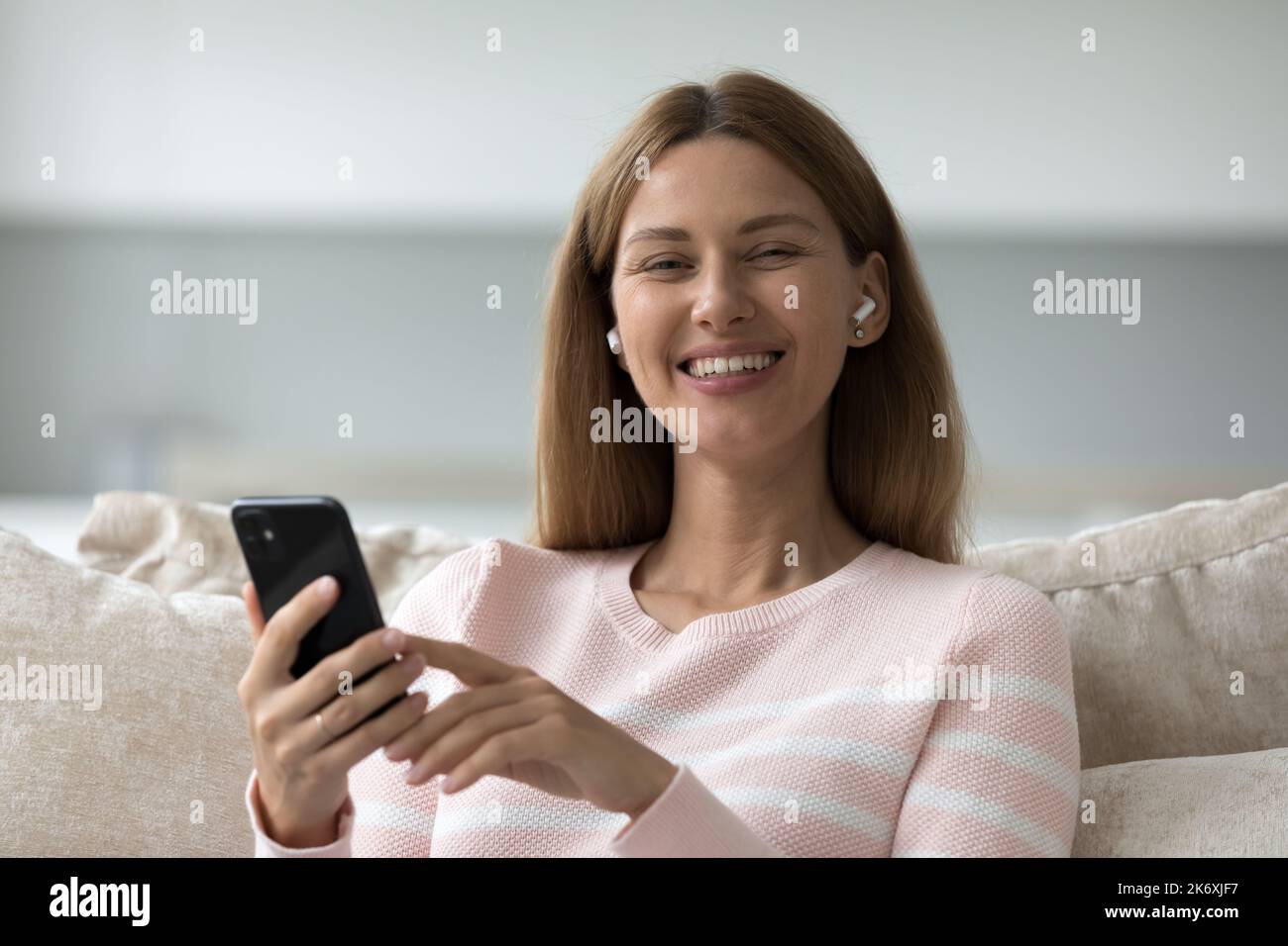 Attraktive Frau ruhen auf Sofa Tragen Sie drahtlose Kopfhörer hält Smartphone Stockfoto