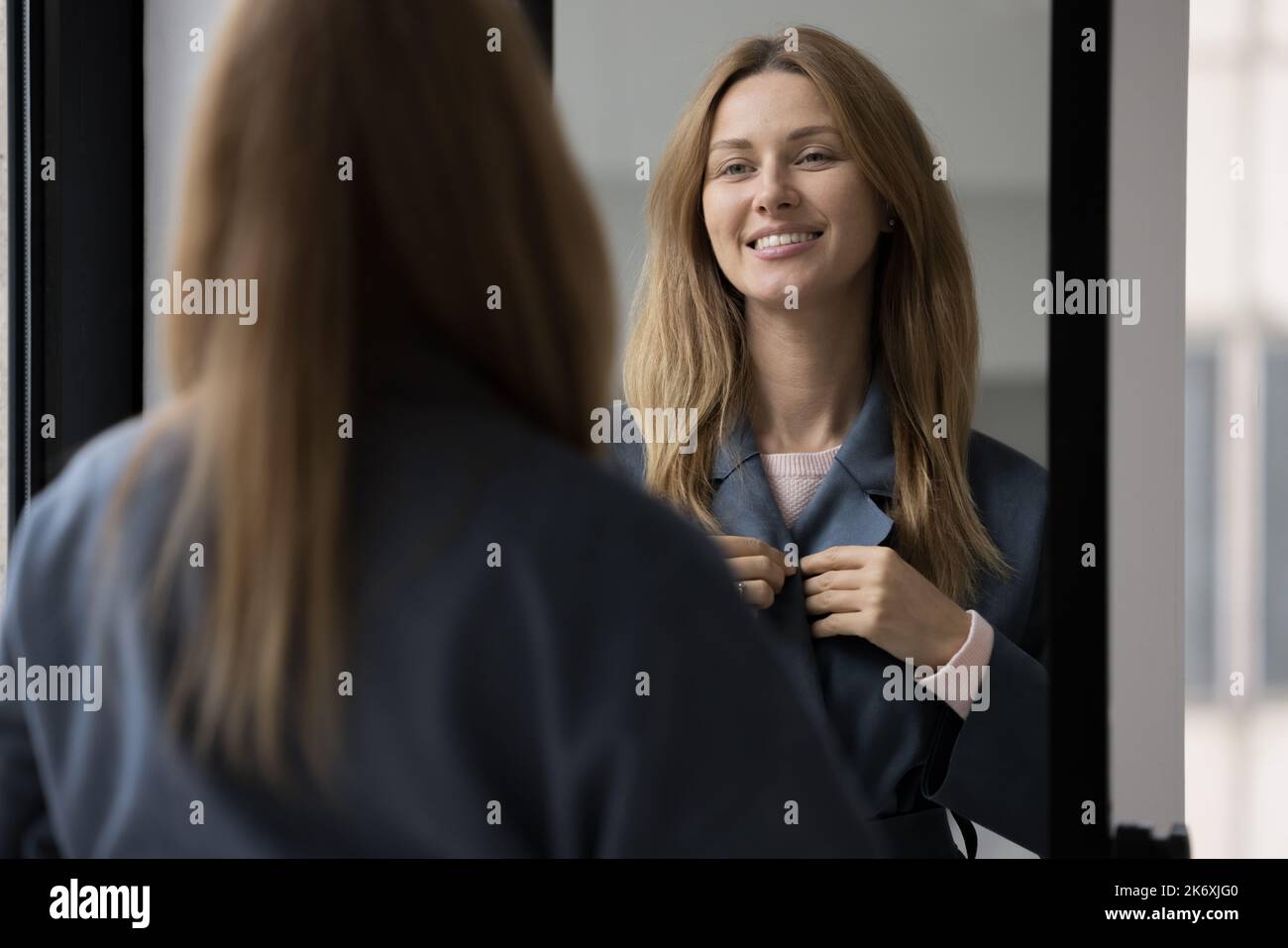 Frau trägt dunklen Casual Mantel stehen drinnen sieht im Spiegel Stockfoto