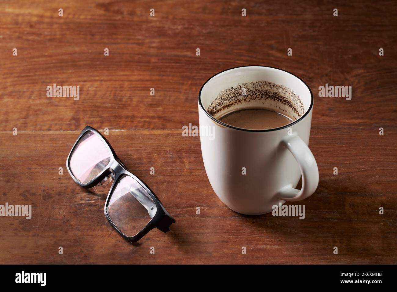 Gebrühter Milchkaffee und Lesebrillen auf einem Holztisch Stockfoto