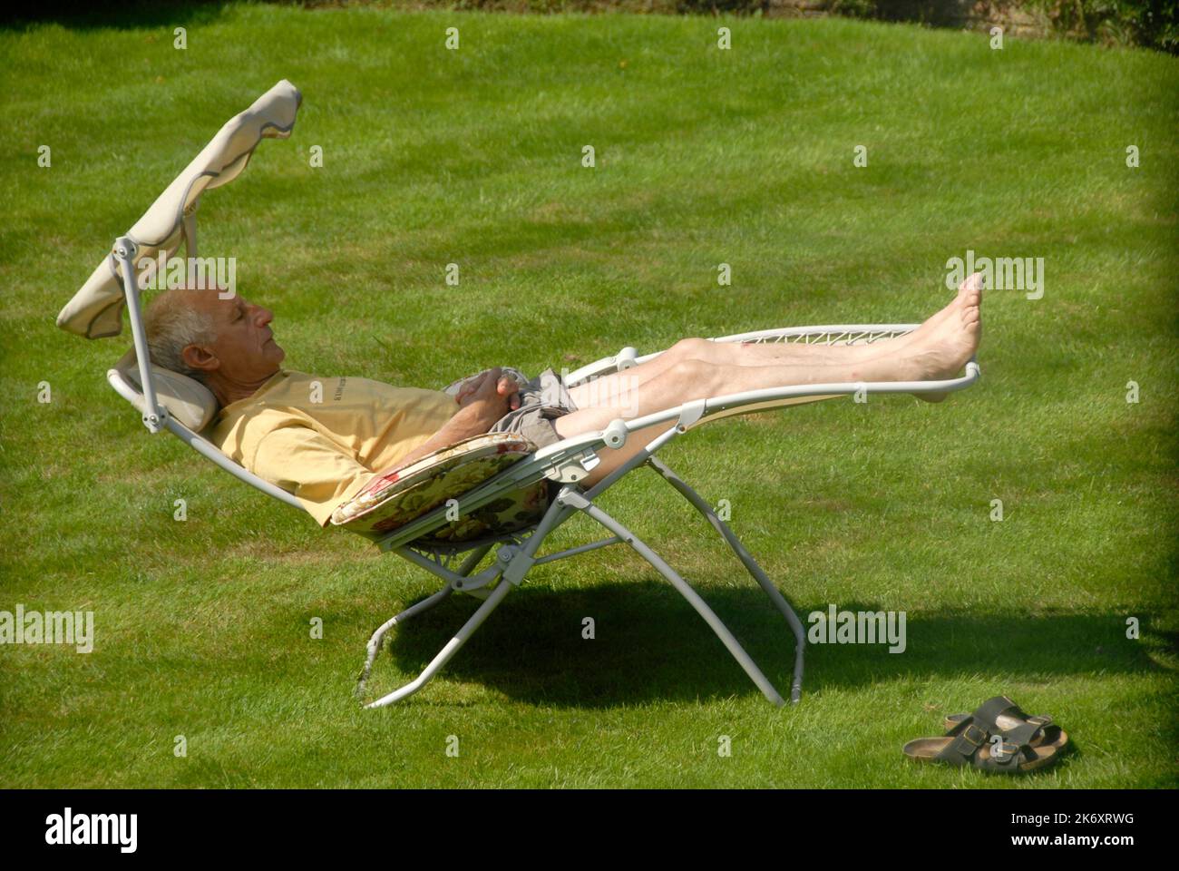 Mann, der sich auf einer Liege im Garten bei warmem Sonnenschein entspannt Stockfoto
