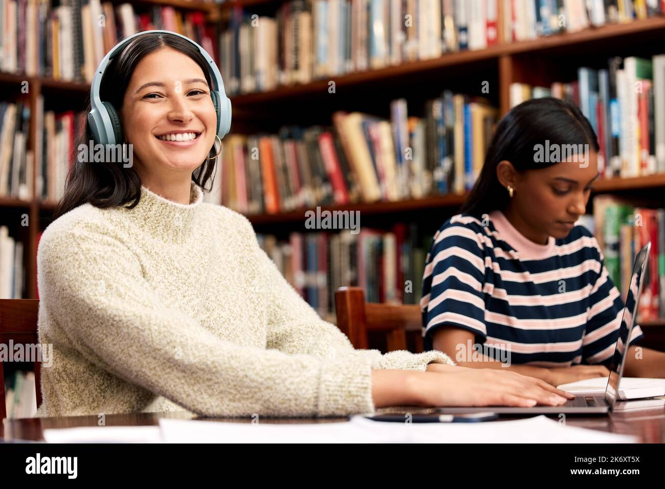 Musik zu hören gibt mir mehr Motivation. Eine junge Studentin, die in einer Bibliothek am College studiert. Stockfoto