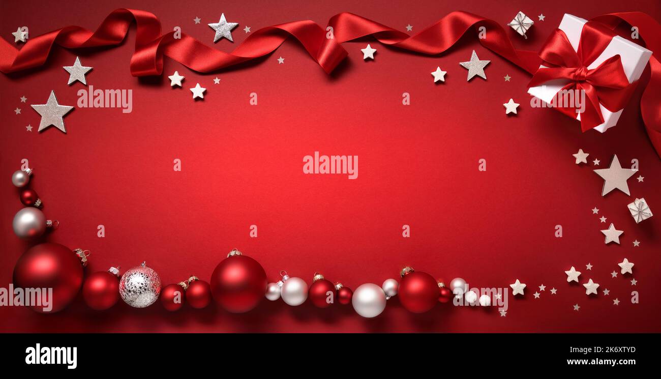 Weihnachtlicher Hintergrund in Rot, mit einem Rahmen aus Kugeln, Geschenkbox, Sternen und Band, der freien großformatigen Kopierraum einrahmt Stockfoto
