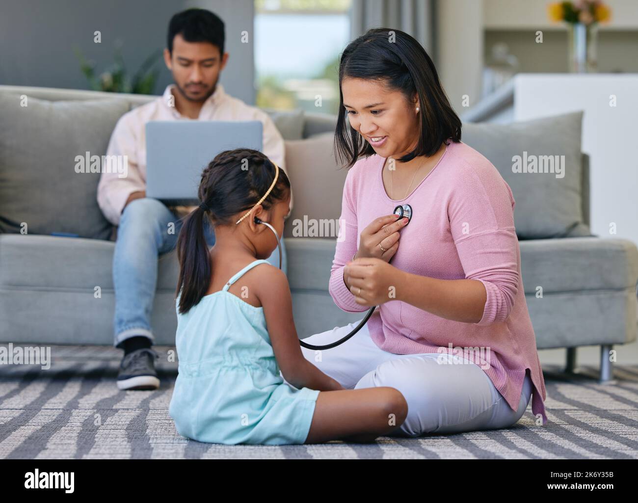 Was hören Sie? Ein junges Mädchen, das spielt, gibt vor, mit ihrer Mutter als Arzt zu arbeiten, während ihr Vater arbeitet. Stockfoto