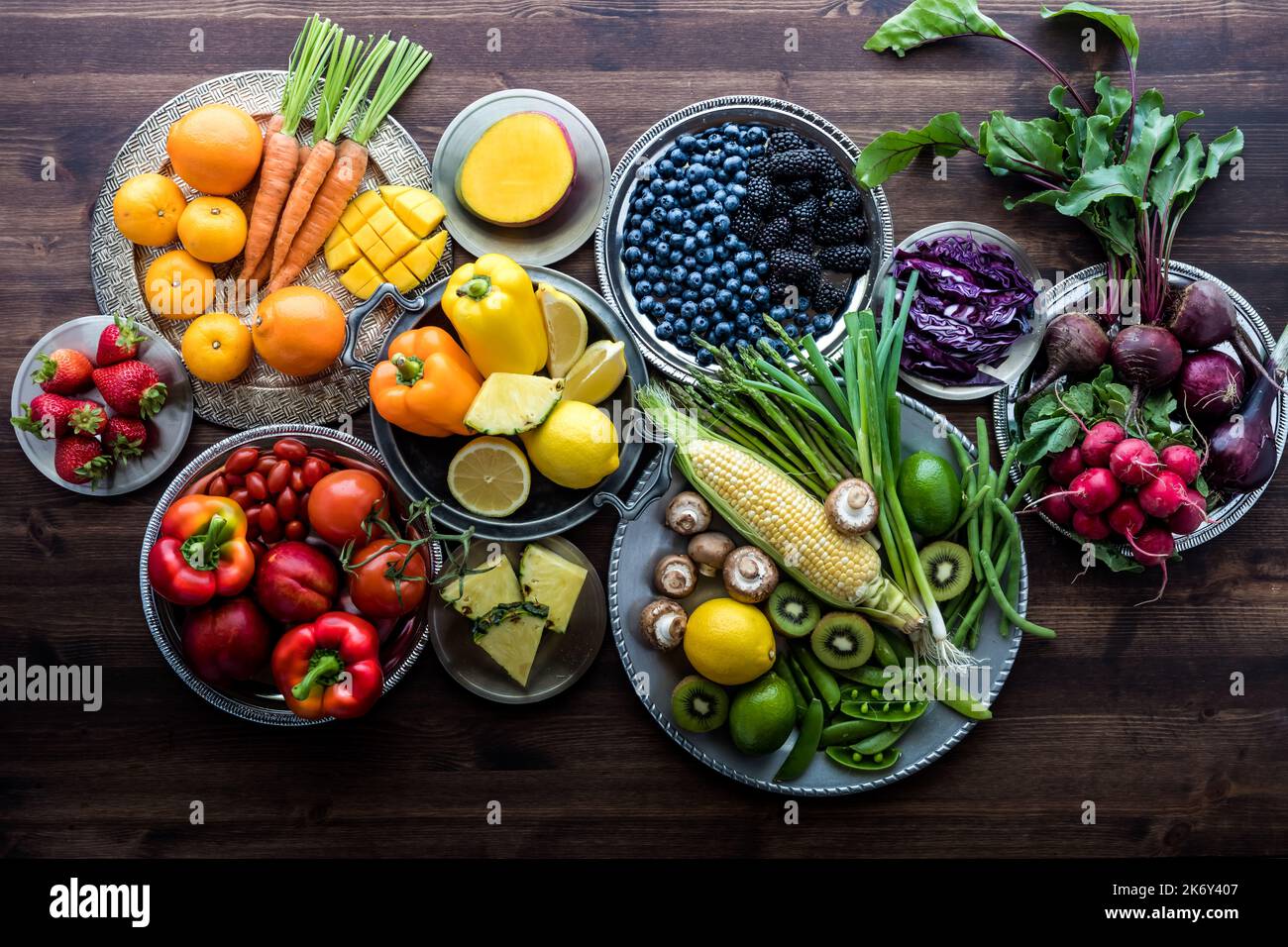 Verschiedene frische Bio-Früchte und -Gemüse auf Metallplatten in Regenbogenfarben vor dunklem Holzhintergrund. Stockfoto