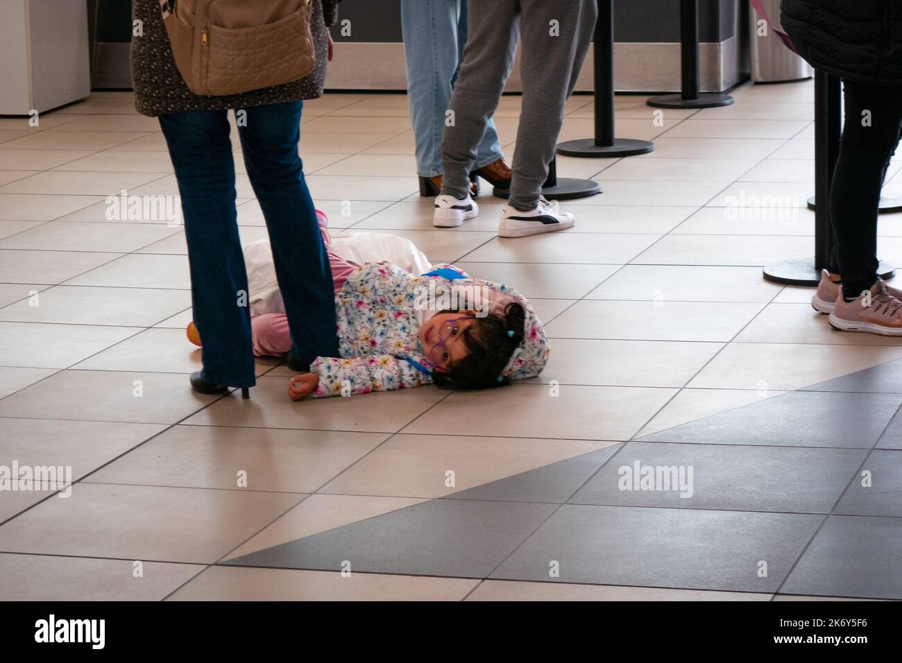 Lima, Peru - 27 2022. Juli: Ein kleines Mädchen, das auf dem Boden im Wartezimmer in der Mitte des Boarding-Bereichs am Flughafen liegt Stockfoto