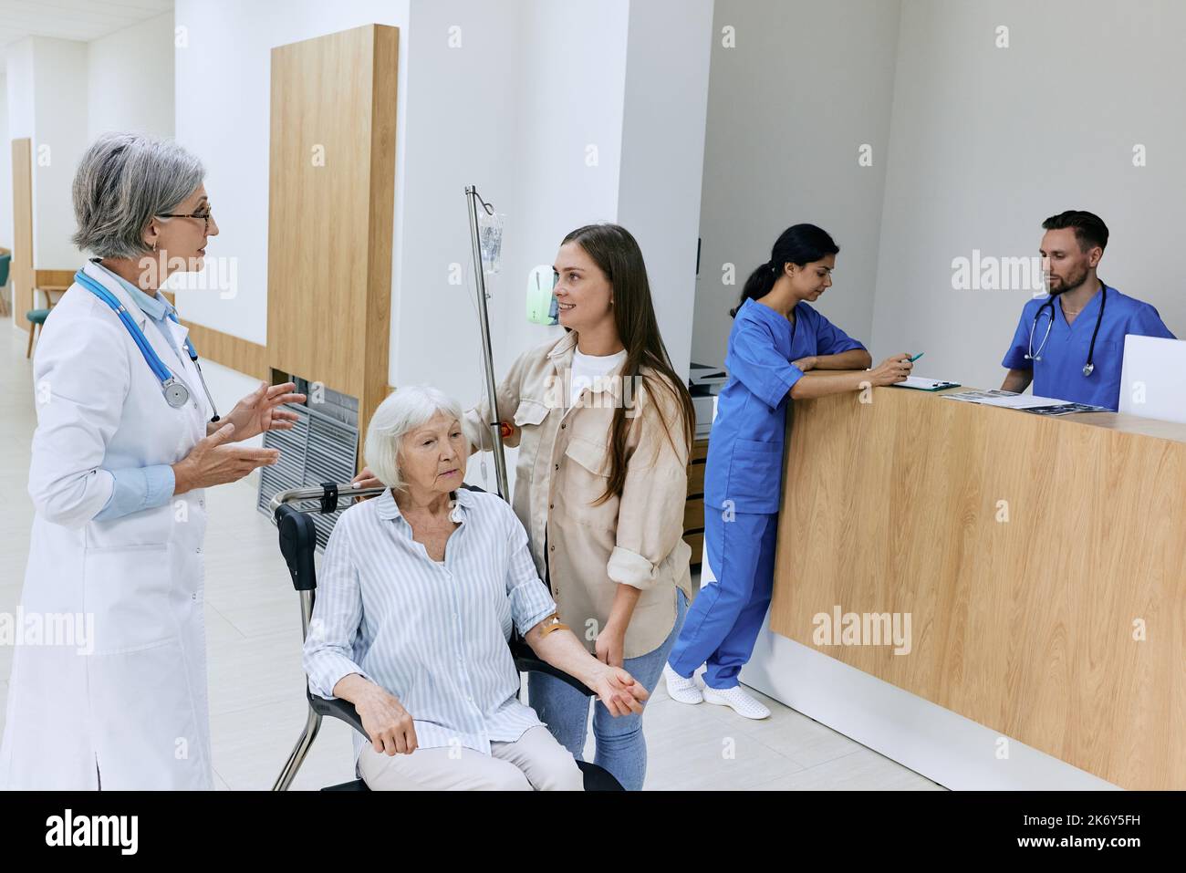 Patientenversorgung im Krankenhaus. Erfahrener Arzt spricht und berät mit der relativen Frau des Patienten und kümmert sich um die Gesundheit der älteren Frau sitzend auf wh Stockfoto