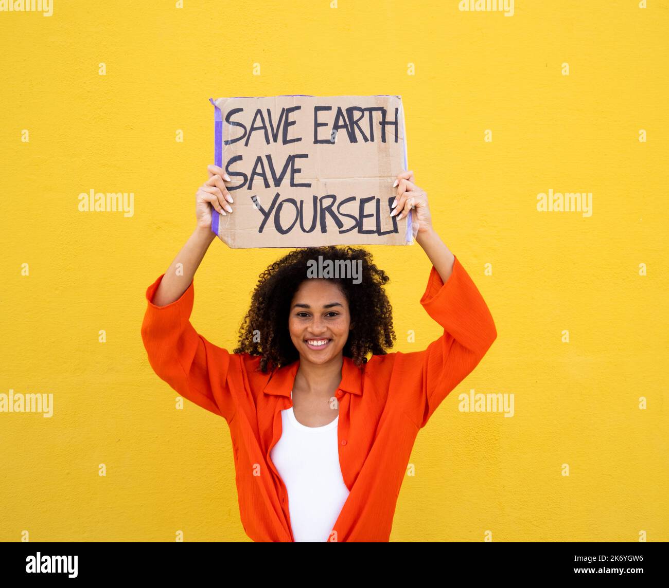 Fröhliche afroamerikanische junge Frau mit einem Schild, das sagt: Rette die Erde rette dich selbst. Umweltschutz, nicht Planet b Stockfoto