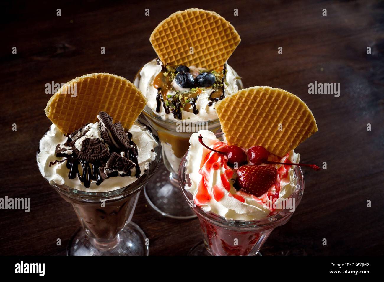 Drei Milchshakes in hohen Gläsern mit Waffeln, Schlagsahne Kirschen, Heidelbeere und Schokolade. Stockfoto