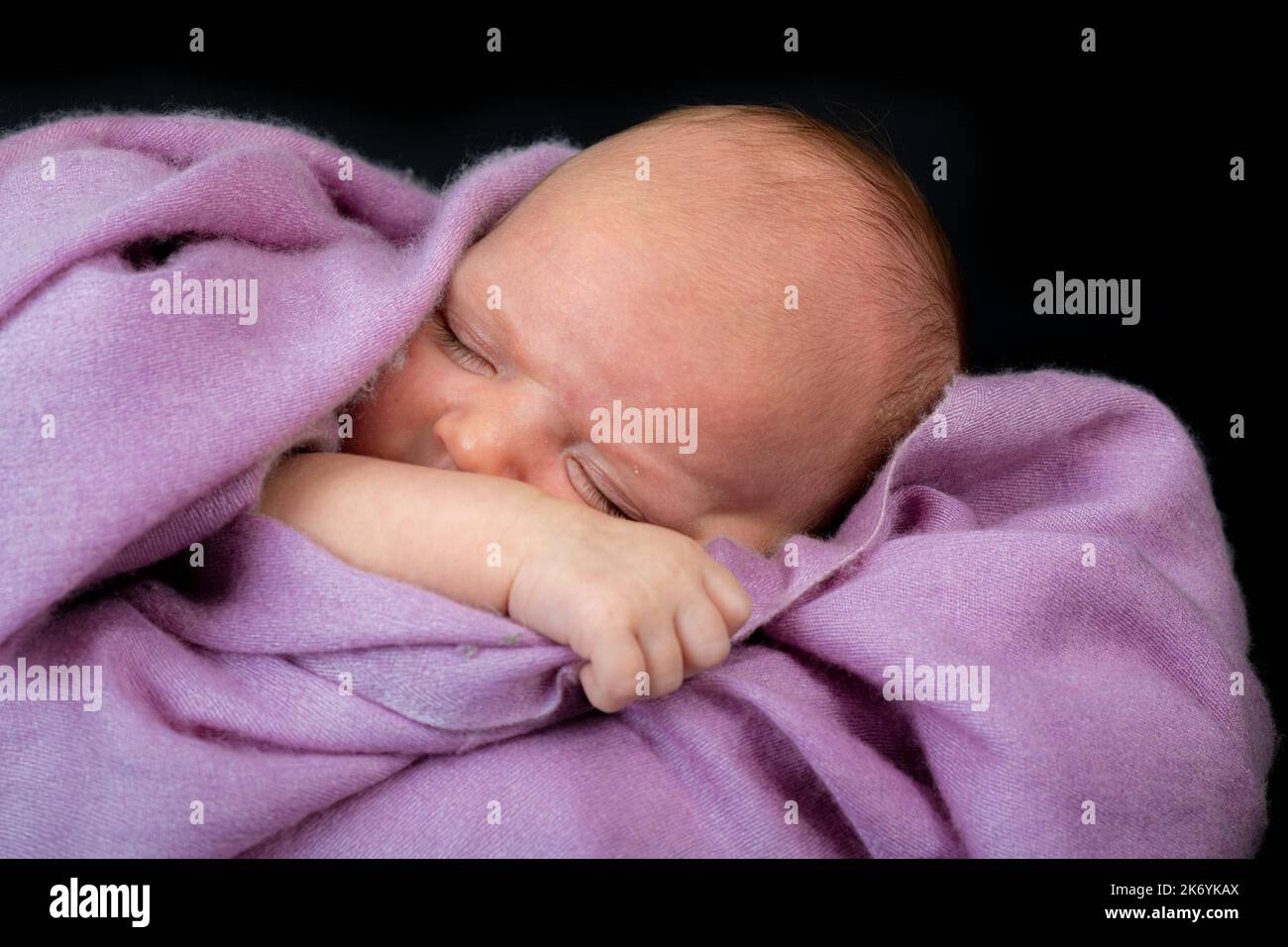 Ein winziges Baby schläft auf einer fliederfarbenen Kaschmirdecke Stockfoto