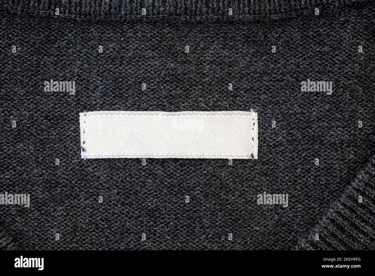 Leerer Streifen, Etikett für Branding auf Pullover. Tag-Mockup auf grauem Tuch, Draufsicht. Stockfoto