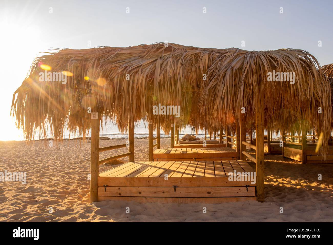 Sonnenliegen mit Palmendach an einem mediterranen Strand mit Sonnenlichtzreifen Stockfoto