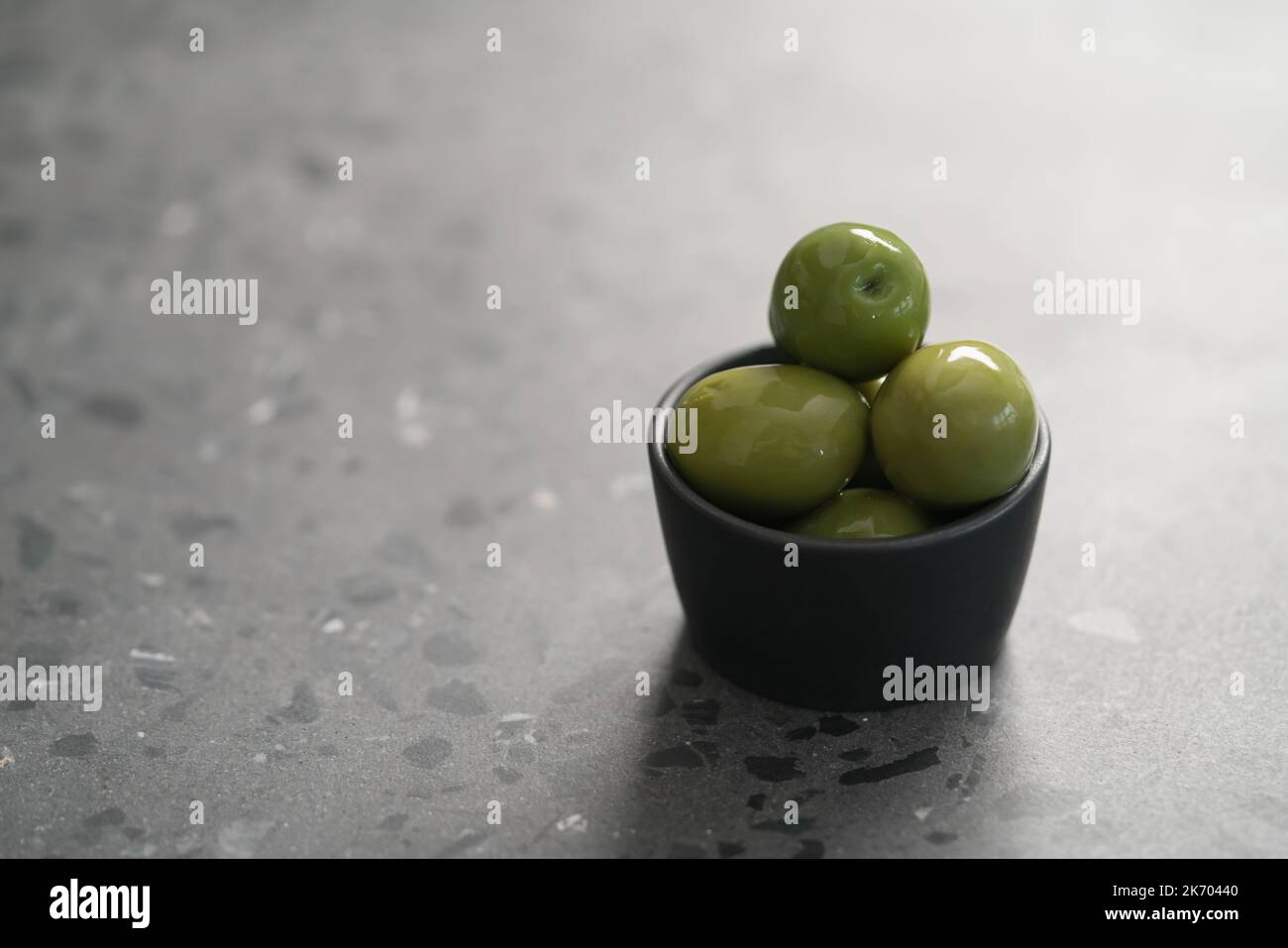 Große grüne Oliven in schwarzer Schale auf Beton Hintergrund, flacher Fokus Stockfoto