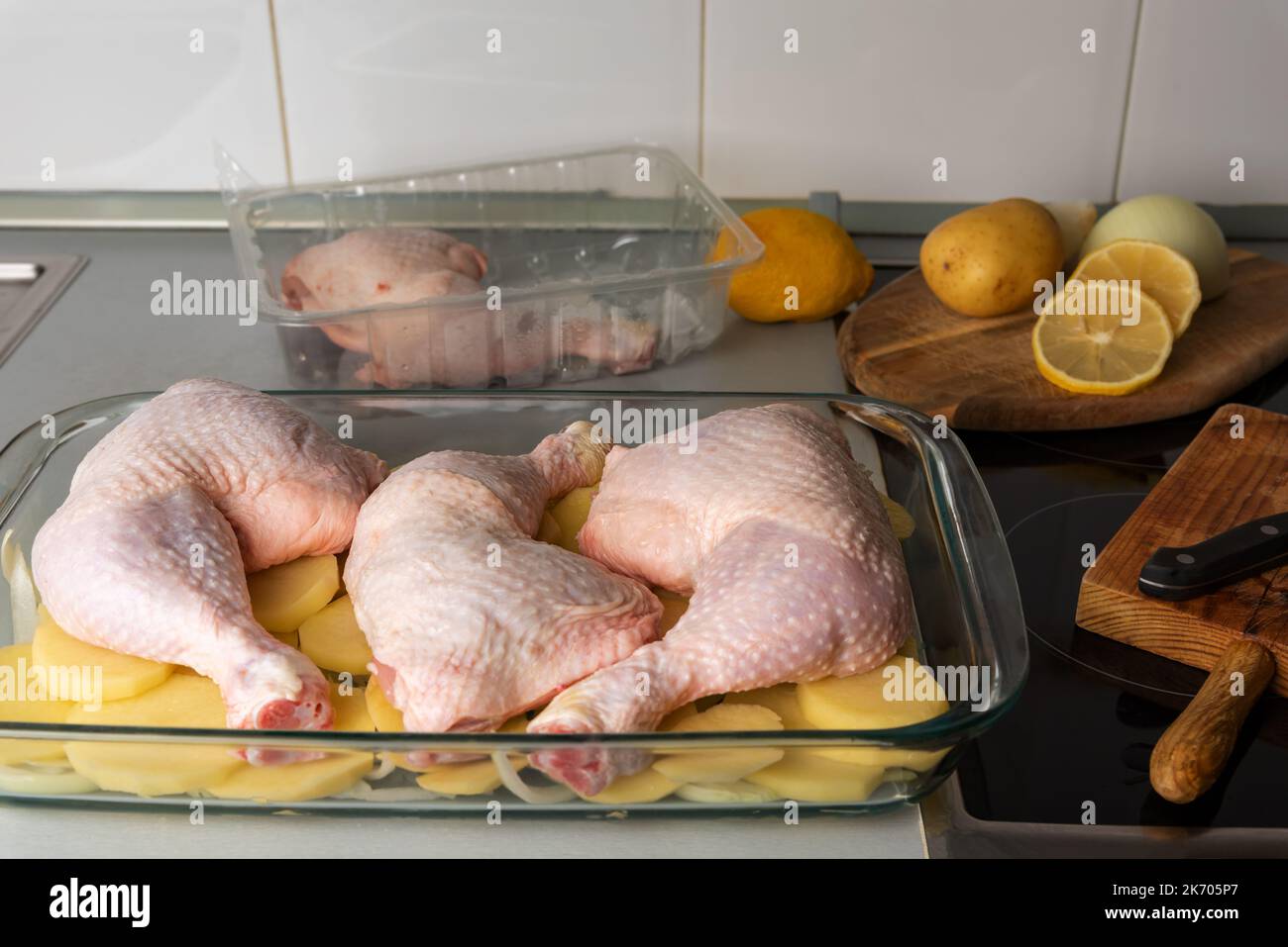 Backblech mit drei Hähnchenschenkeln auf einem Kartoffelbett und gehackten Zwiebeln. Stockfoto