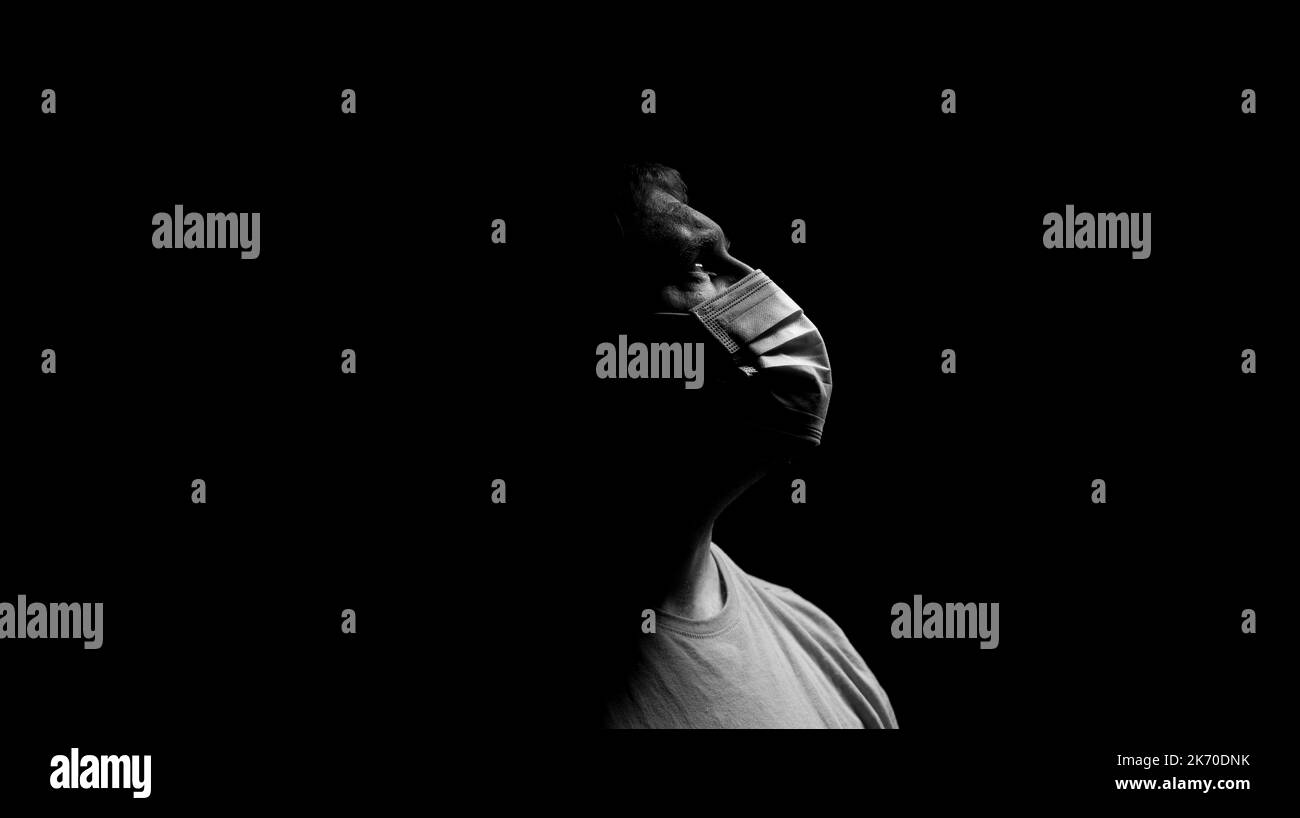 Mann, der eine OP-Maske trägt und in einem dunklen Raum nach oben blickt. Stockfoto