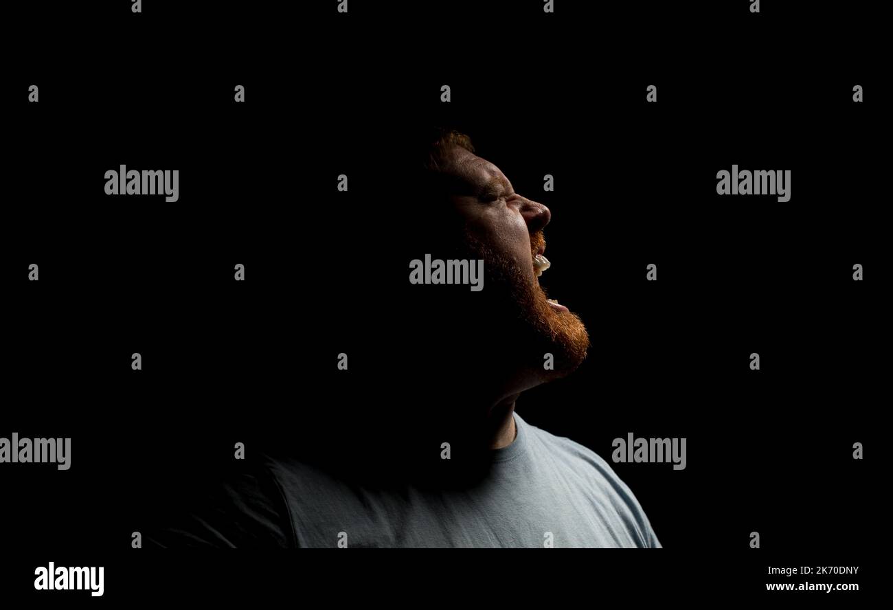 Seitenkopfaufnahme eines Mannes, der in einem dunklen Raum schreiend/schreiend ausdrückt. Stockfoto