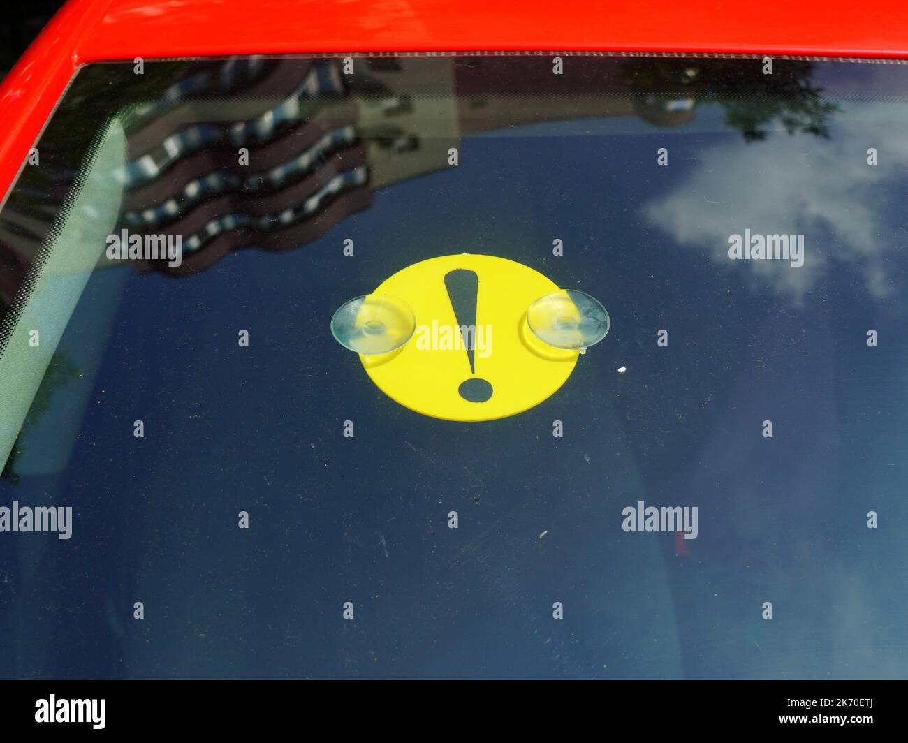 Anfänger Fahrer Ausrufezeichen gelb auf roten Auto Windschutzscheibe und Reflexion von Block von Wohnungen und Himmel Stockfoto