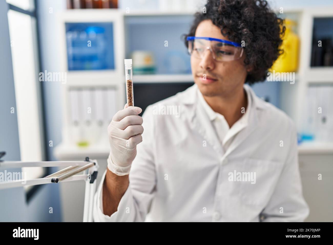 Junger hispanischer Mann in Wissenschaftleruniform mit Klemmbrett und Reagenzglas im Labor Stockfoto