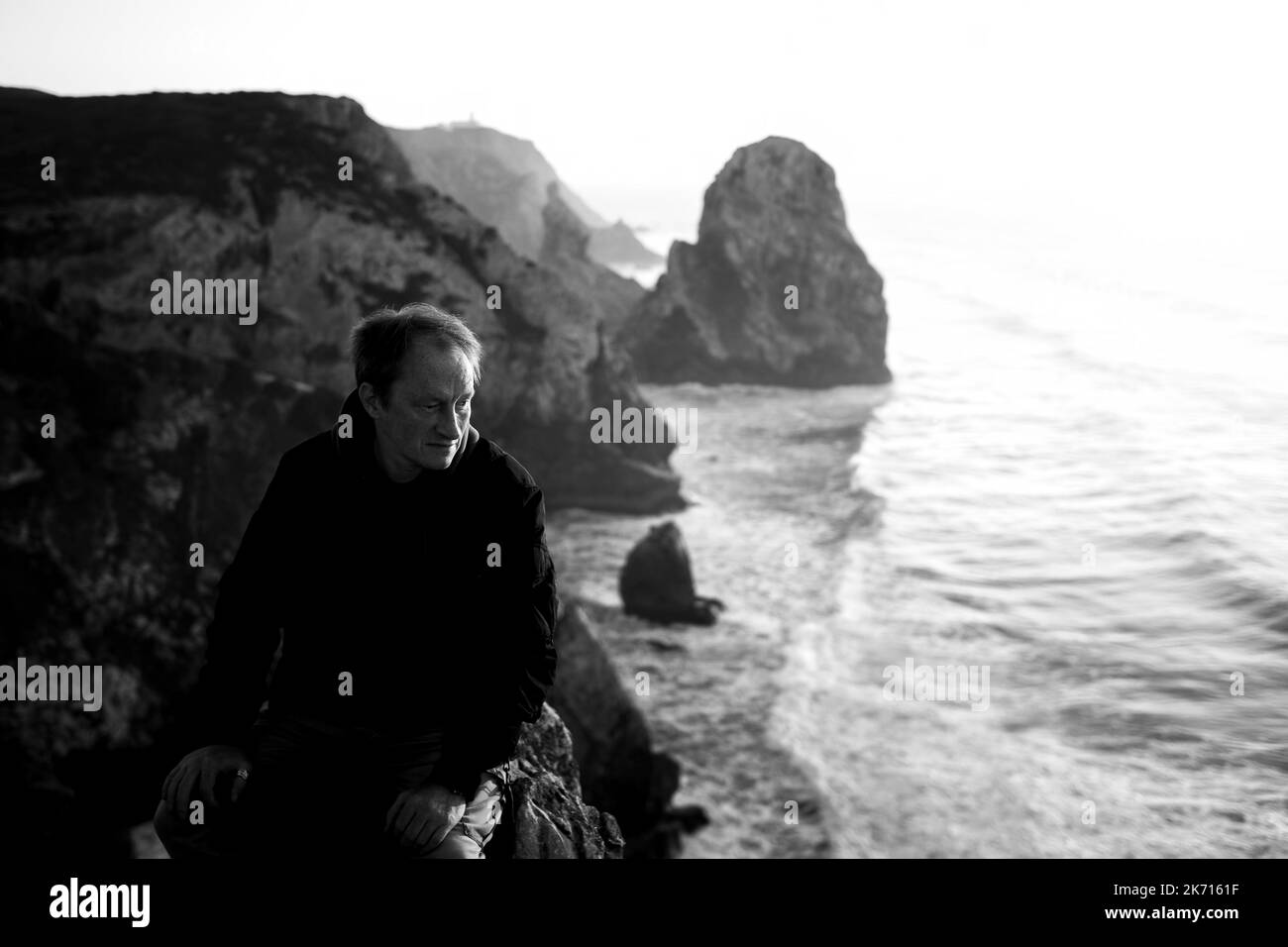 Ein Mann sitzt am Rande eines Felsens von Cabo da Roca, Atlantica, Portugal. Schwarzweiß-Foto. Stockfoto