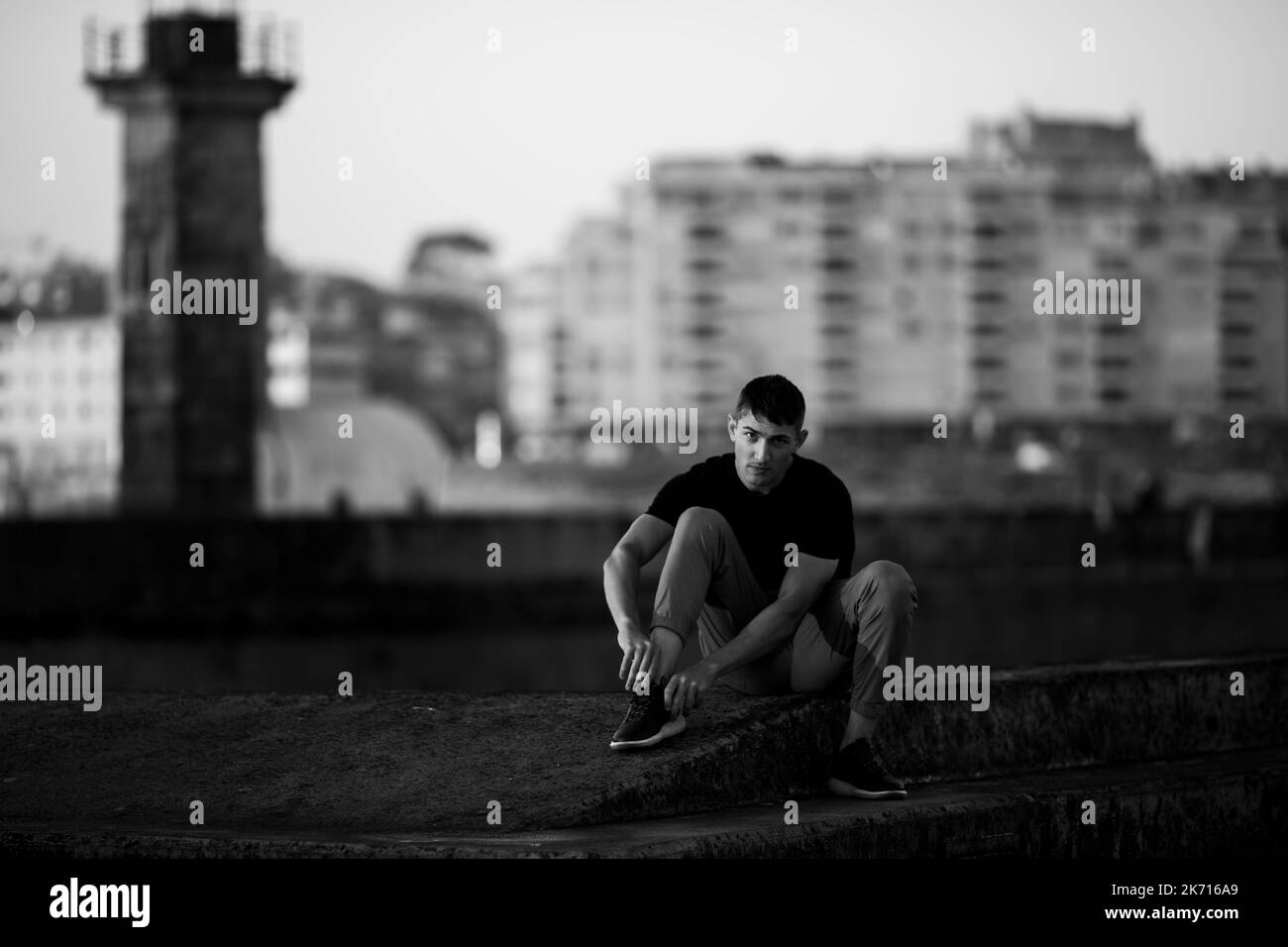 Ein junger Mann sitzt am Meer und schnürt seine Schuhe. Schwarzweiß-Foto. Stockfoto