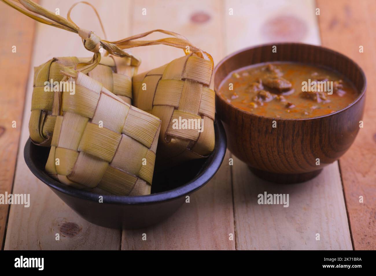 Ketupat (Reisknödel) und ein Stück mit einem kleinen Stück auf Holzboden. Ketupat ist ein natürlicher Reiskörper aus jungen Kokosblättern zum Kochen von Reis während eid Mu Stockfoto