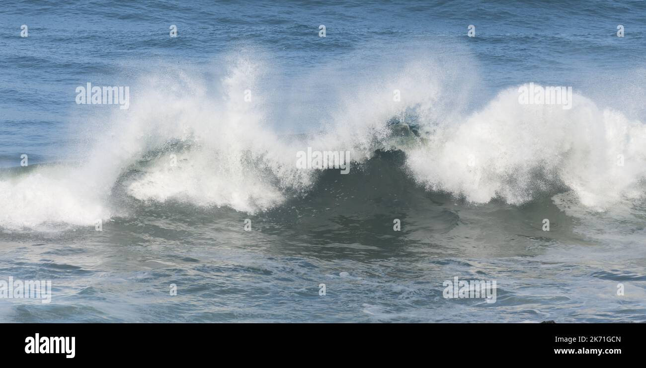 Ozeanwelle stürzt in einem Zustand der zufälligem Verwirrung gegen blaues Wasser ab Stockfoto
