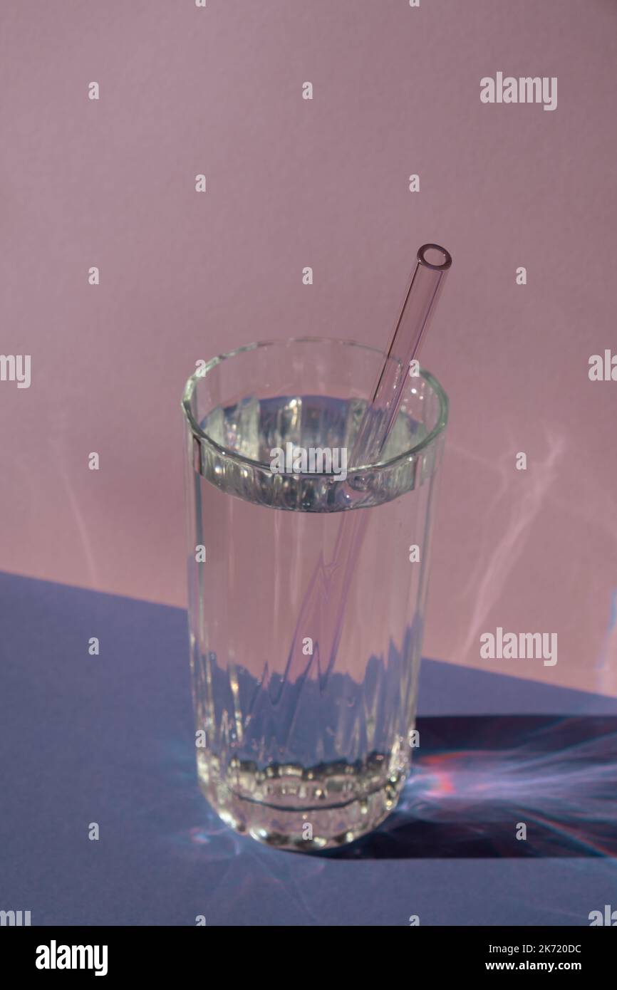 Wiederverwendbares Glas Strohhalme in Glas mit Wasser auf violettem Hintergrund umweltfreundliches Trinkhalm-Set mit Reinigungsbürste. Zero Waste, plastikfreies Konzept. Nachhaltiger Lebensstil. Waste free living geringer Abfall Stockfoto