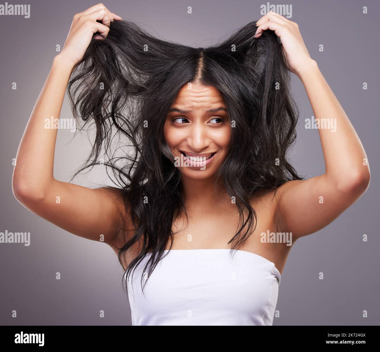 Ich komme näher an die Rasur heran. Eine attraktive junge Frau, die allein im Studio steht und sich gestresst fühlt, während sie auf ihre Haare schaut. Stockfoto