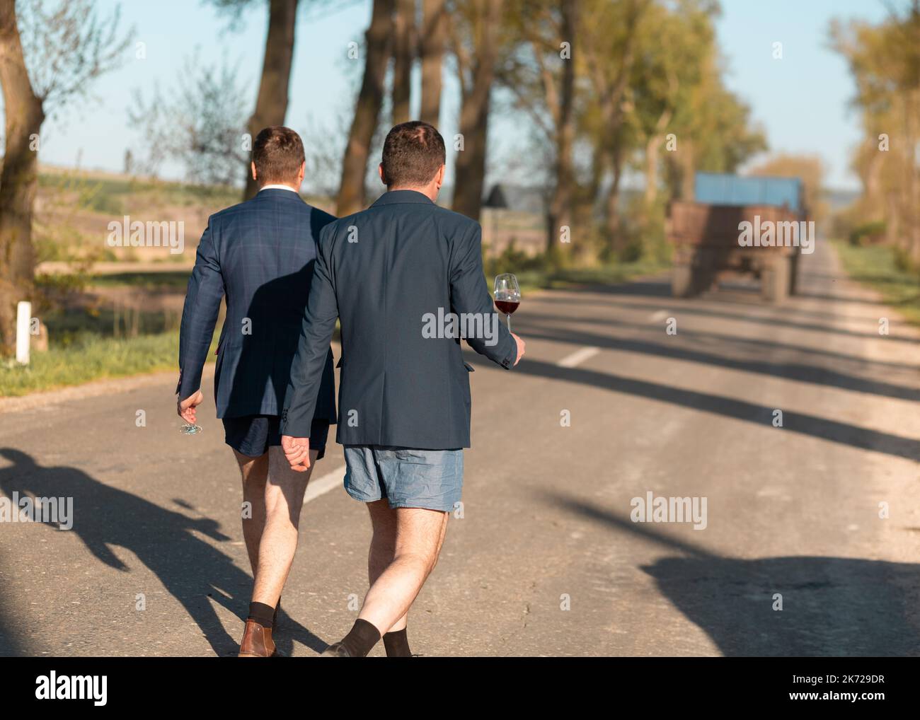 Zwei kaukasische Männer gehen in Jacke und Unterhose mit Rotweingläsern Stockfoto