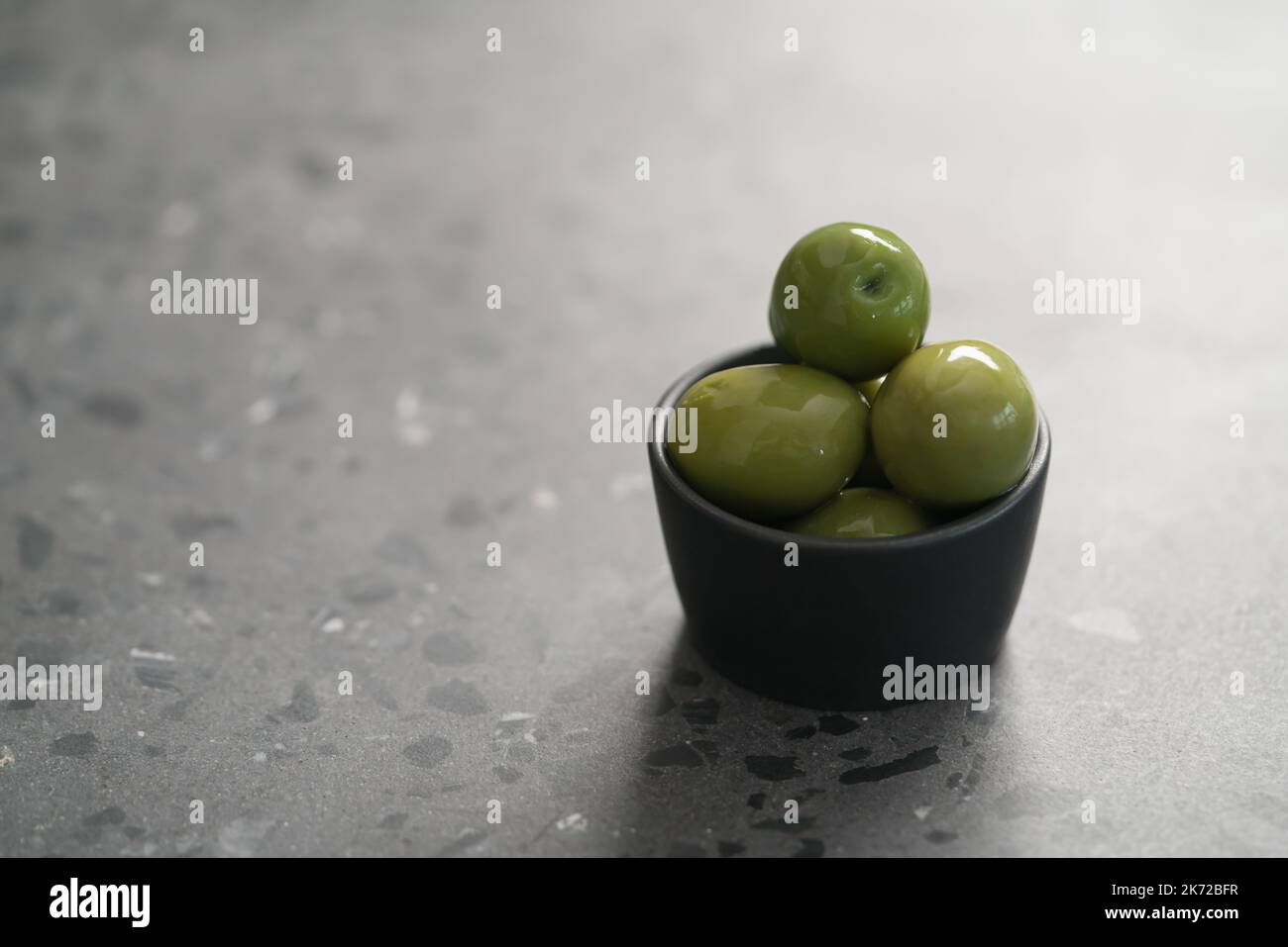Große grüne Oliven in schwarzer Schale auf Beton Hintergrund, flacher Fokus Stockfoto