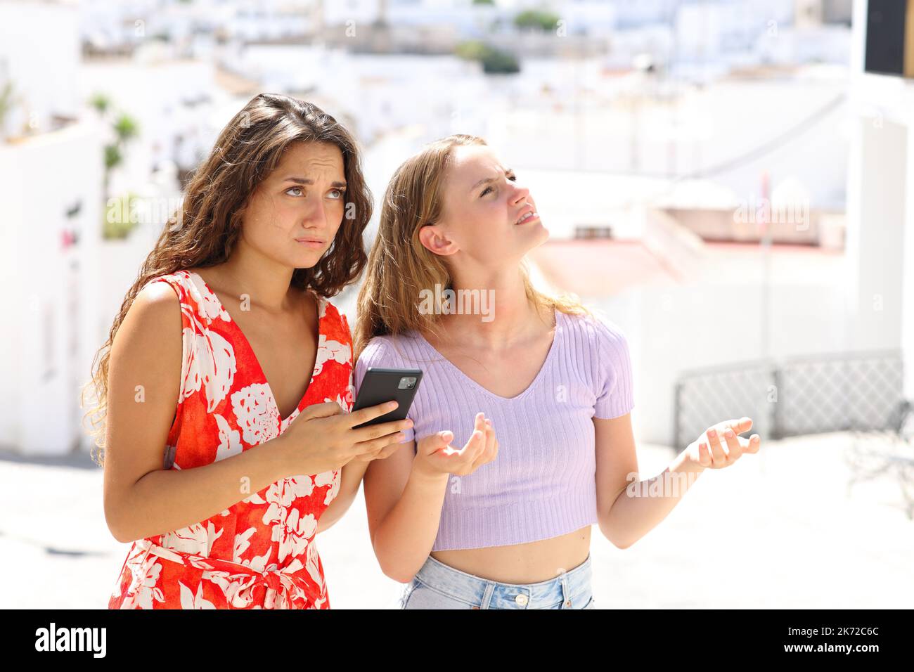 Verlorene Touristen, die in den Sommerferien in einer weißen Stadtstraße ihren Standort auf einem Smartphone nachsehen Stockfoto