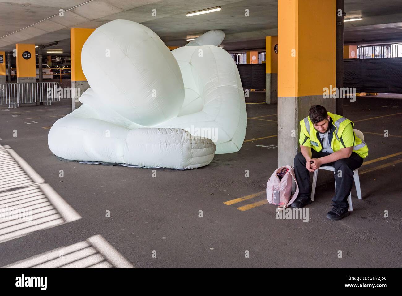 Ein Sicherheitsbeamter wartet auf Menschenmengen, die beim Parramatta Lanes Festival ankommen, neben einem riesigen aufblasbaren Humanoid auf einem Parkplatz in Parramatta Stockfoto