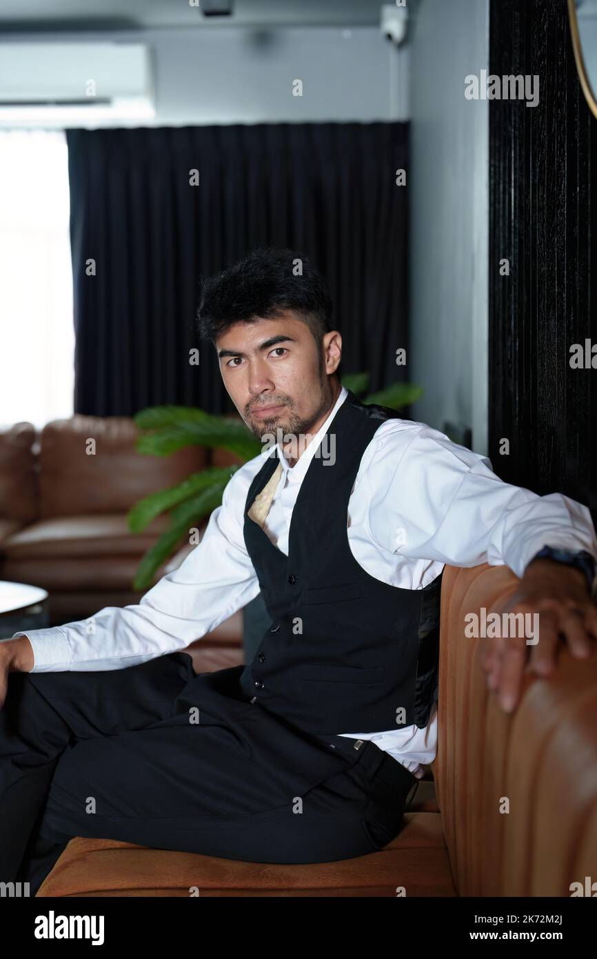Porträt eines gut aussehenden asiatischen Mannes, der auf dem Sofa sitzt Stockfoto