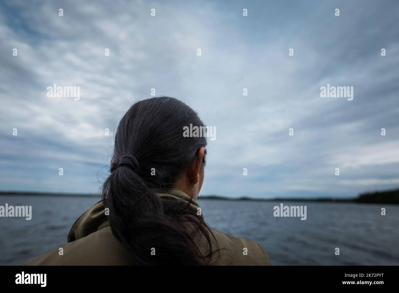 Schwarzhaarige Person, die auf den See schaut Stockfoto
