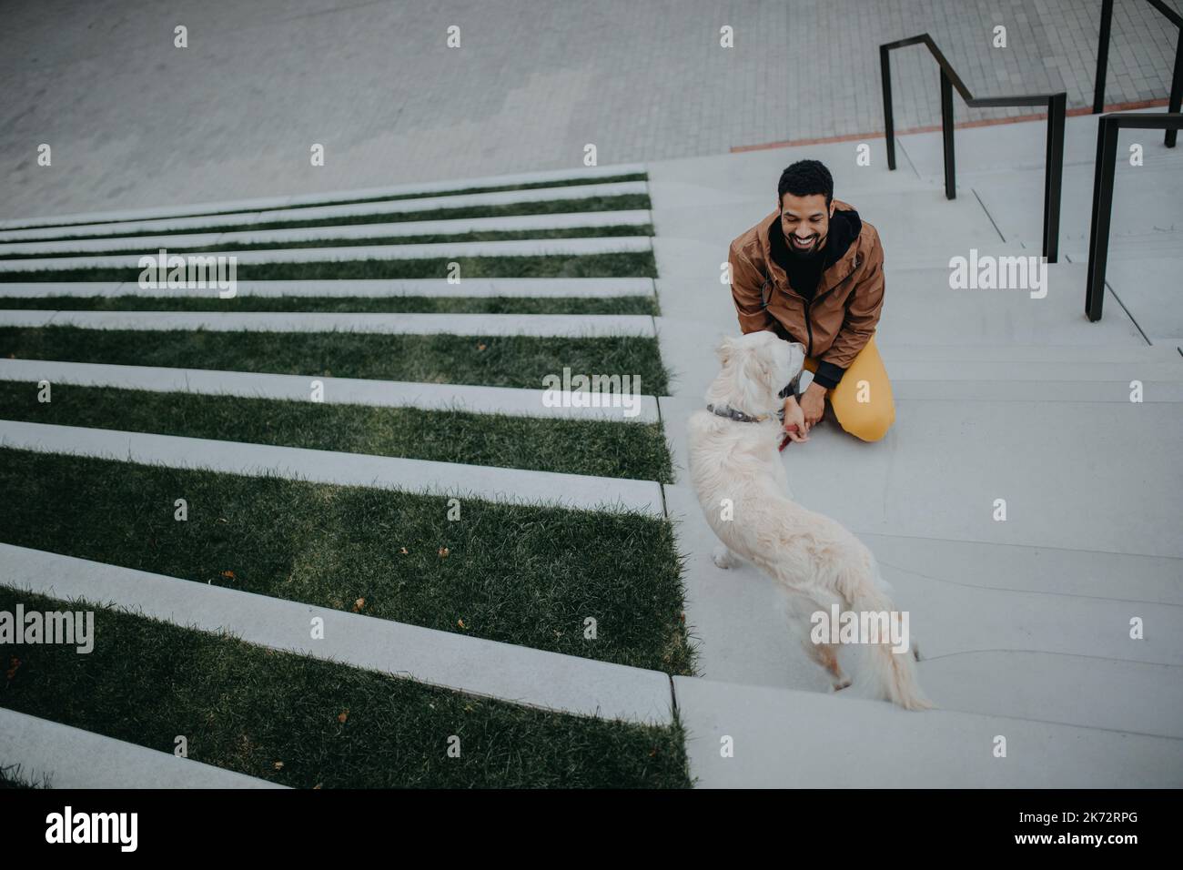 High-Angle-Ansicht des glücklichen jungen Mannes mit seinem Hund im Freien in der Stadttreppe. Stockfoto