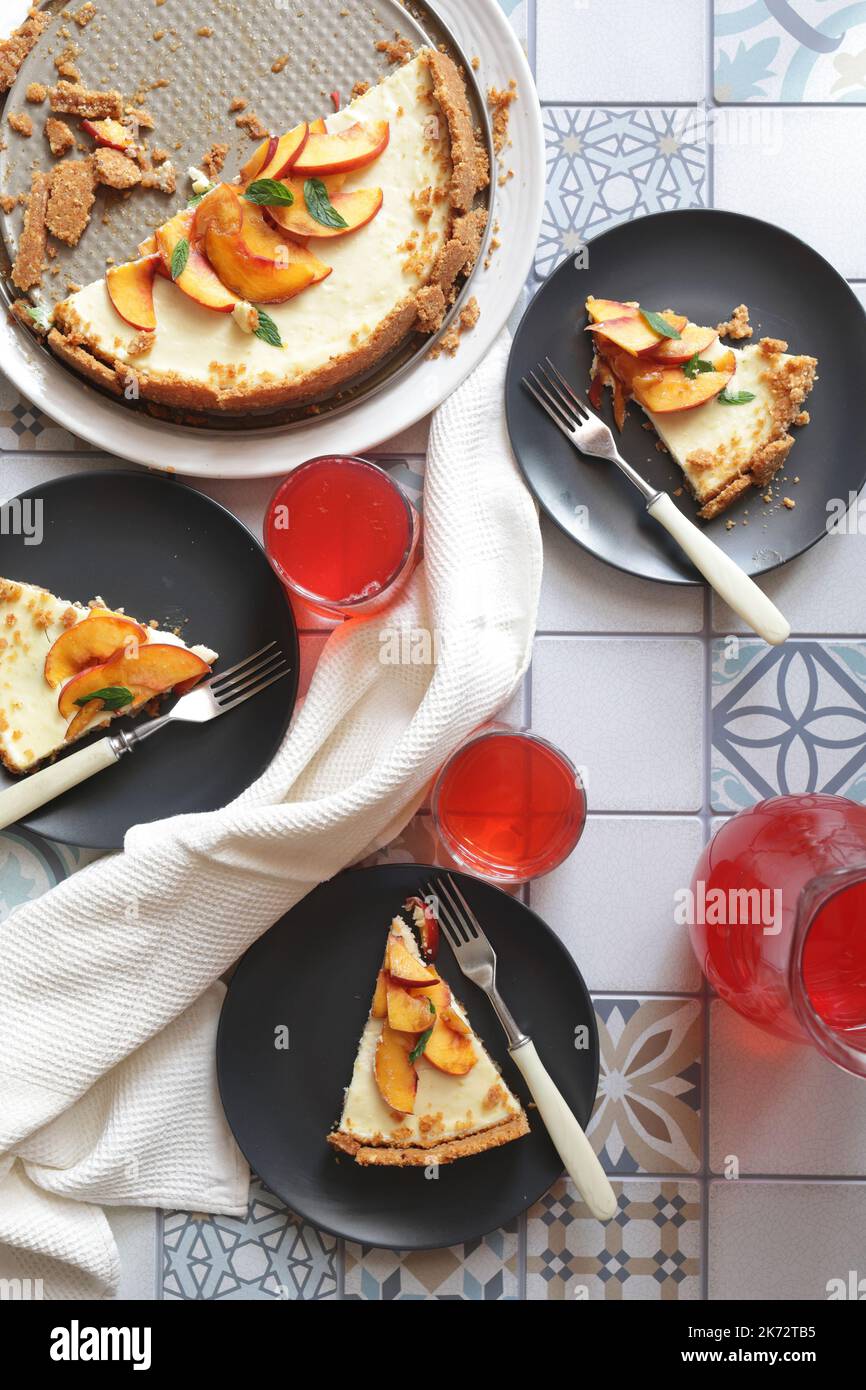 Portionen Ingwer-Tarte mit frischen Pfirsichscheiben auf schwarzen Tellern. Tarte in Portionen mit Krümel schneiden. Beerensaft in Gläsern Stockfoto