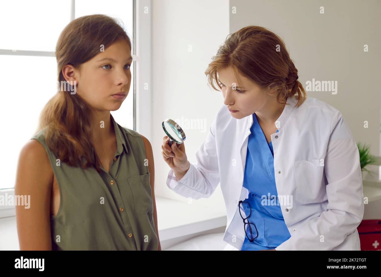 Der Dermatologe schaut durch die Lupe, während er die Haut eines Kinderpatienten untersucht Stockfoto