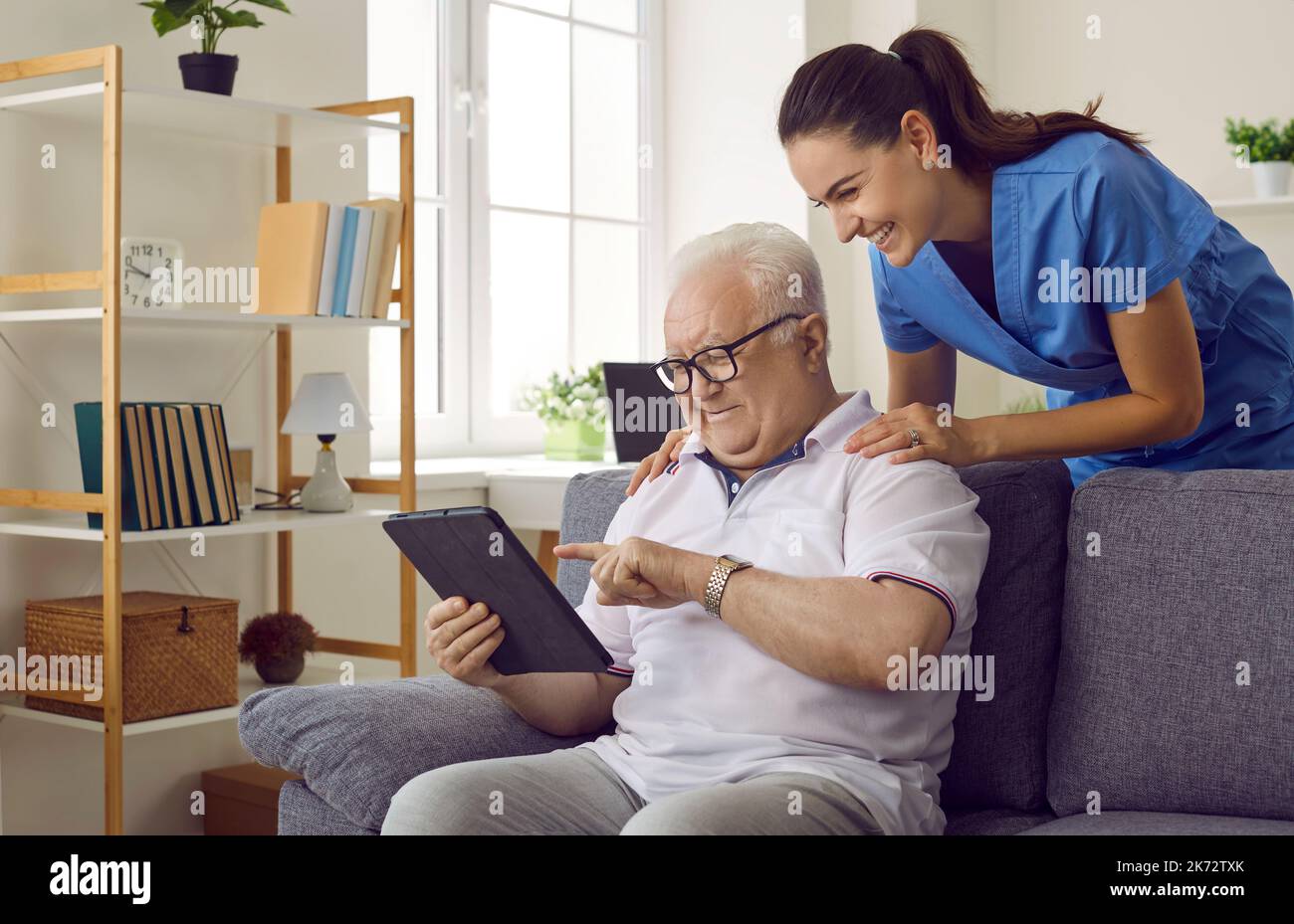 Krankenschwester zeigt dem alten Mann, wie er mit Apps auf einem digitalen Tablet seine Gesundheit überwachen und E-Books lesen kann Stockfoto