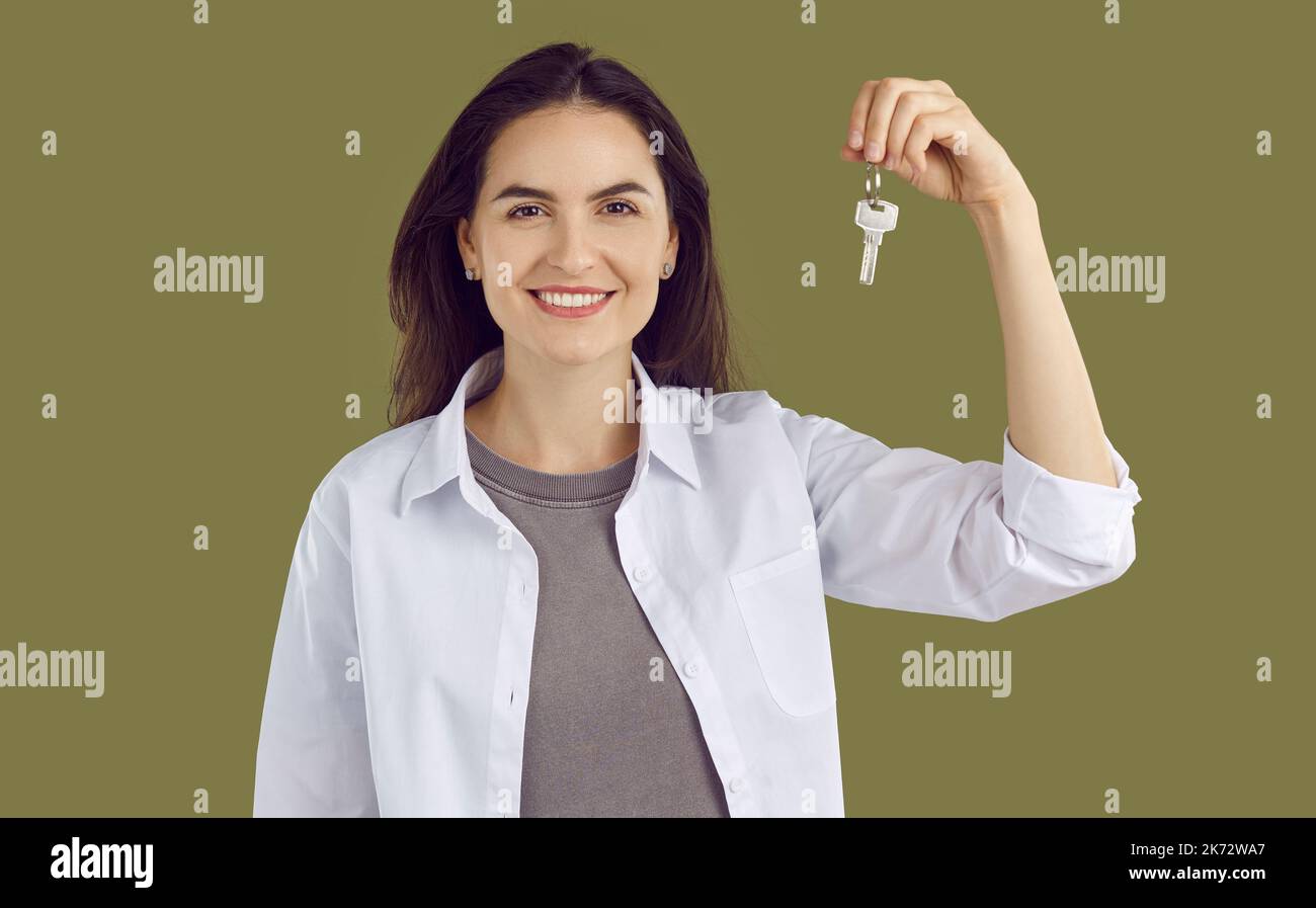 Junge lächelnde Brünette Frau in einem weißen Hemd hält Schlüssel in der Hand auf khaki Hintergrund. Stockfoto
