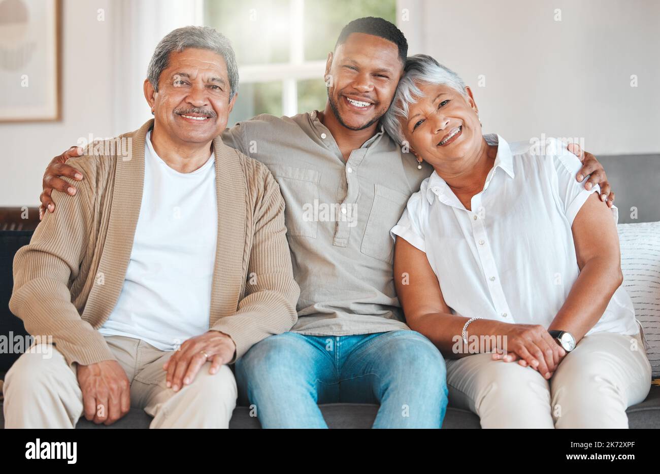 Meine Eltern, mein Schatz. Porträt eines reifen Paares, das sich mit seinem Sohn zu Hause auf dem Sofa verklebt. Stockfoto